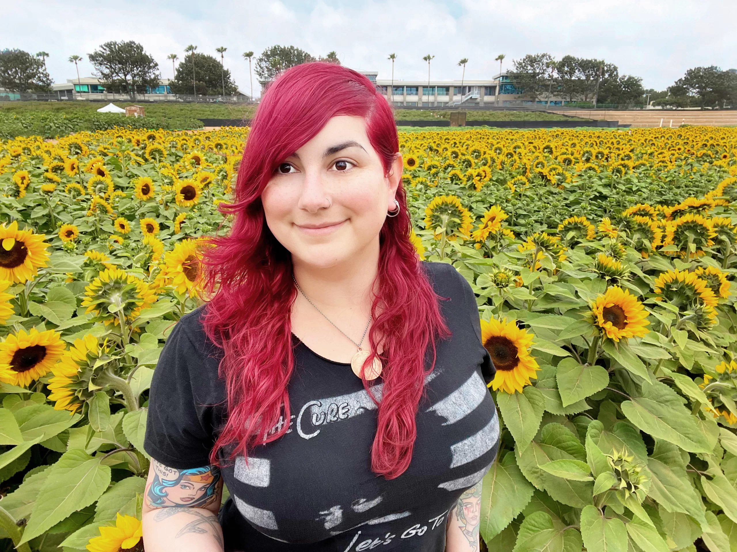 A photo of Kitty in a field of sunflowers. She is wearing a black t-shirt with an image of the band, The Cure. 
